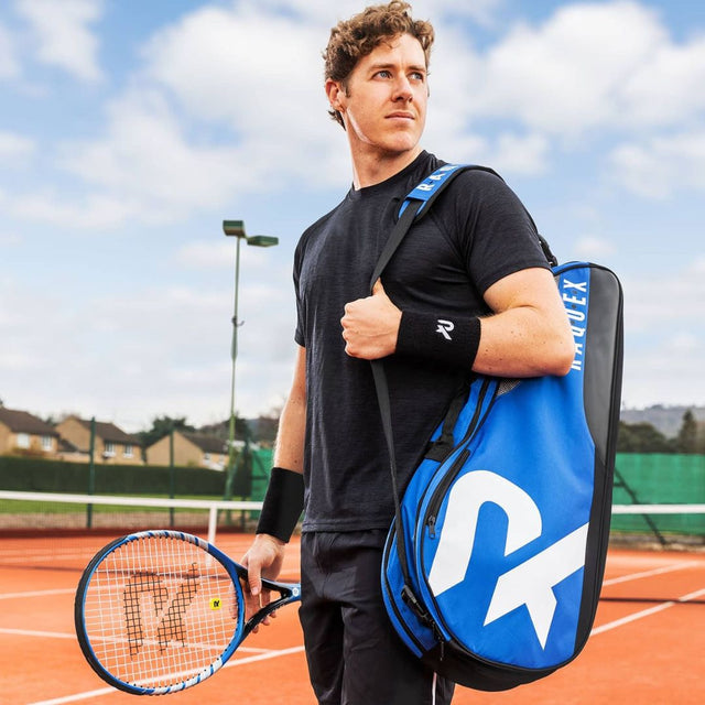 A man on a clay tennis court carrying the Blue and black Racquet bag from Raquex