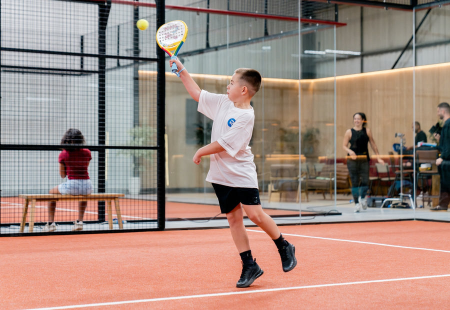 A boy mid-rally on an indoor padel court playing with a coloured-in Raquex x Crayola junior racquet