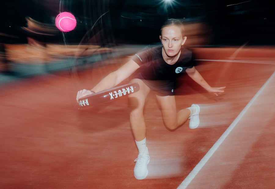 Padel player lunging low to reach a pink Raquex padel ball on an indoor court