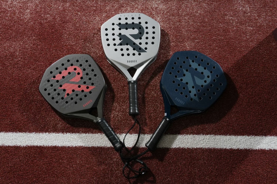 Three Raquex padel racquets in grey, silver and navy laid out on a red court