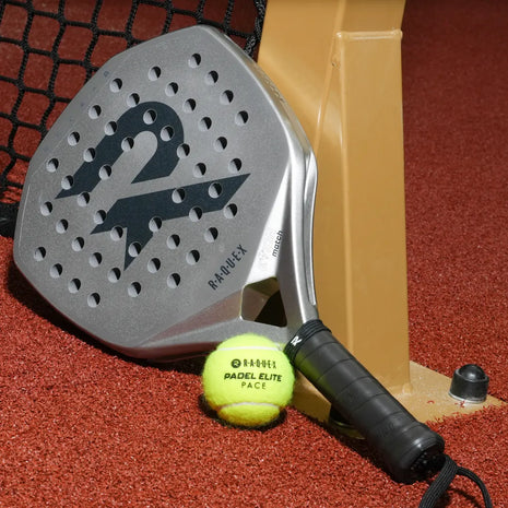 Raquex Evion Match padel racquet in silver resting against a padel net post, with a Raquex Padel Elite Pace ball on the red court