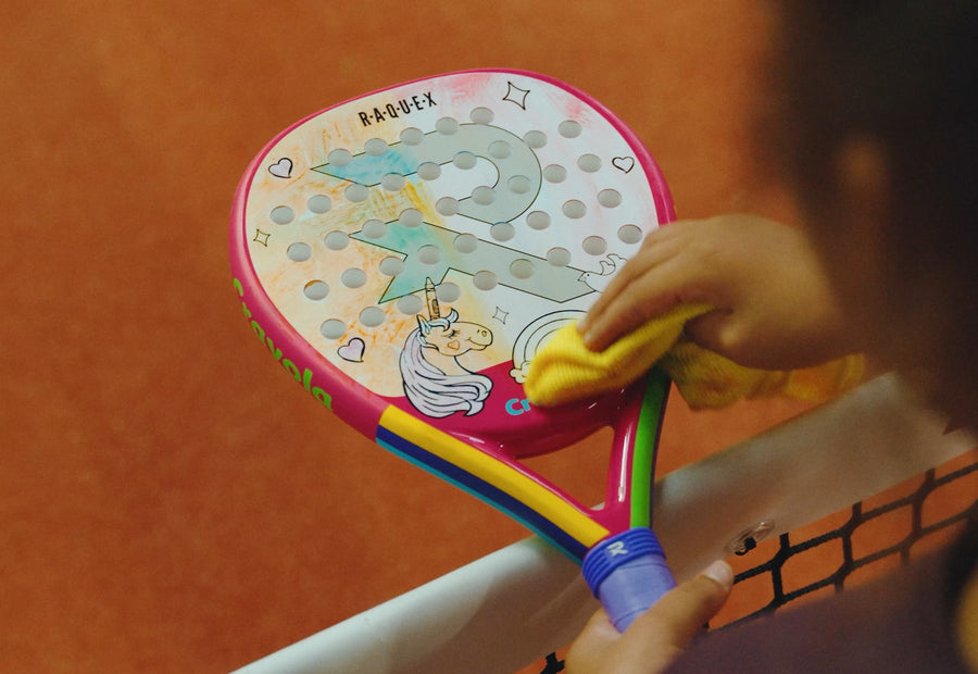 A Raquex x Crayola racquet being wiped clean with a yellow cloth at the net, half of the unicorn design already gone