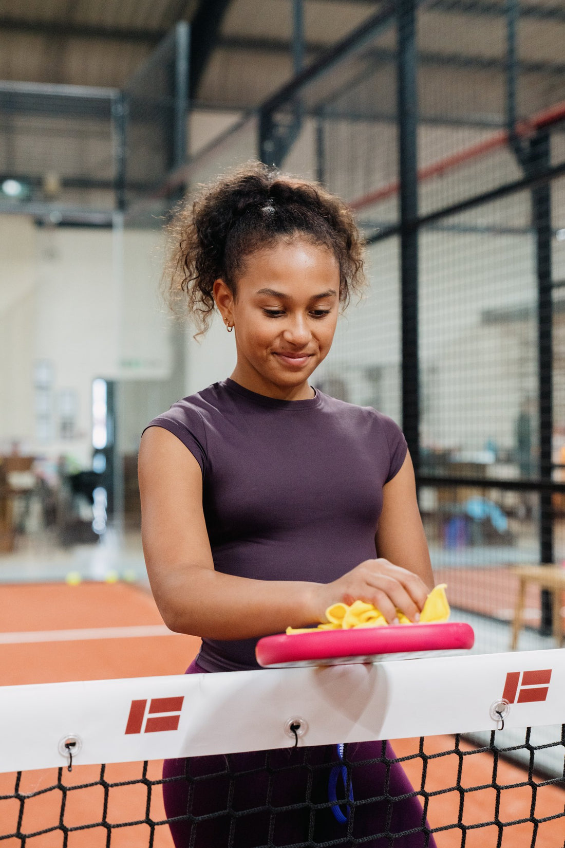 A girl at the net of an indoor padel court wiping her coloured-in Raquex x Crayola racquet clean with a yellow cloth