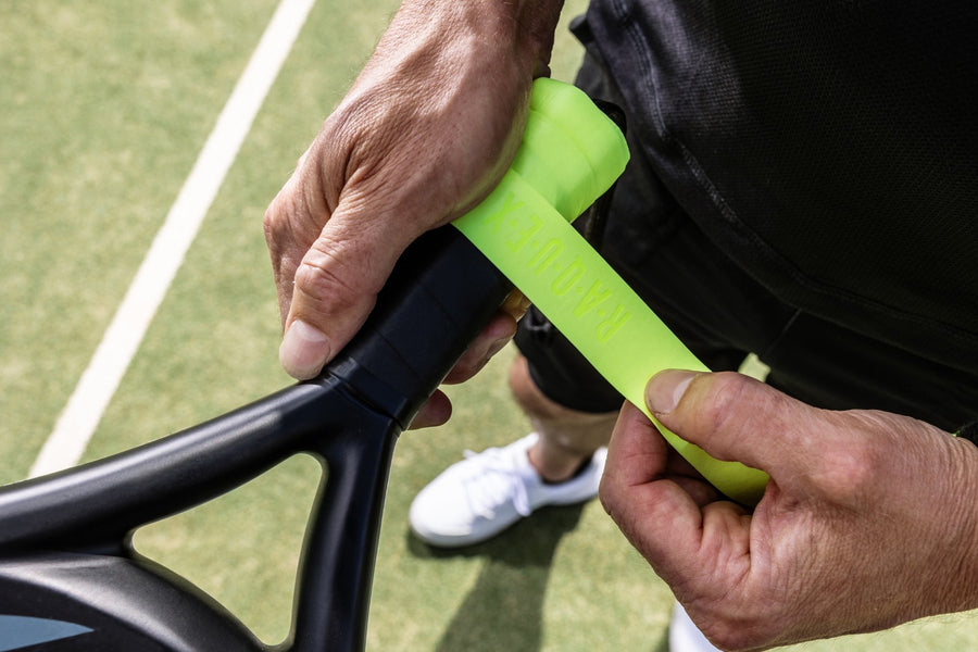A player wrapping a neon green Raquex overgrip onto a racquet handle on court