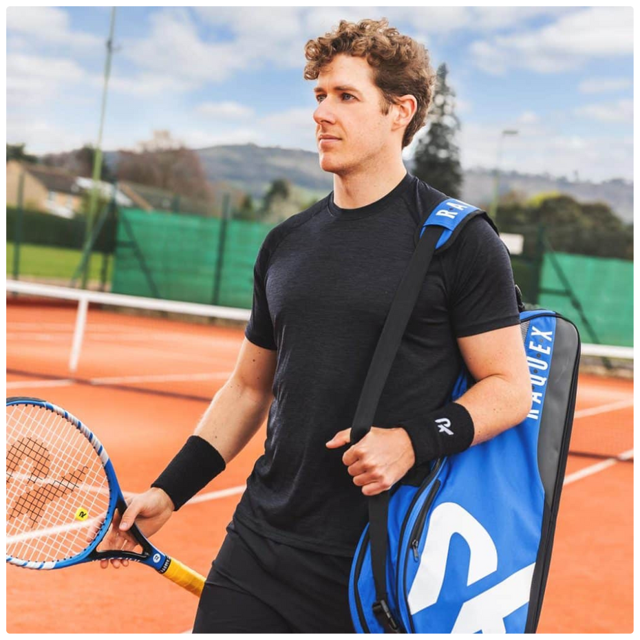 A man on a clay tennis court holding a Raquex bag and racket