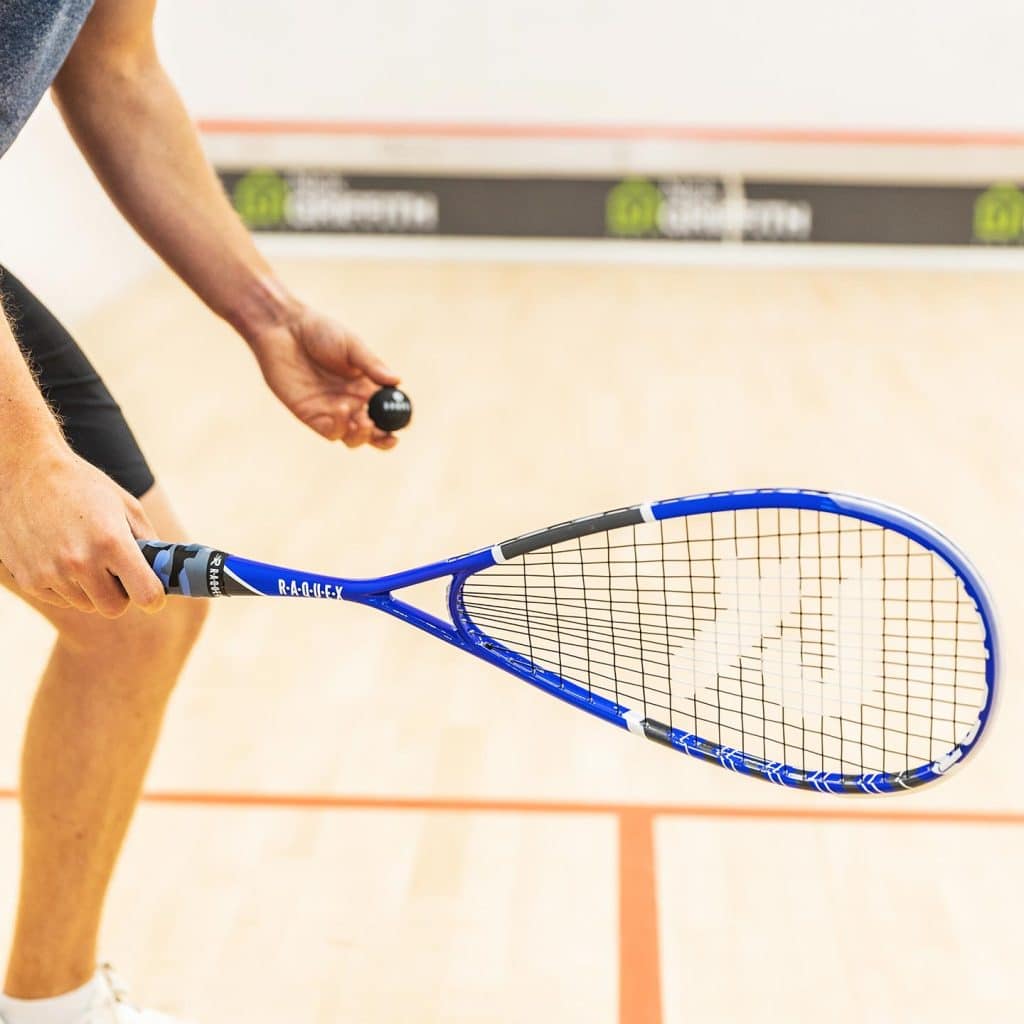 Man on a squash court with a blue squash racquet and black squash ball