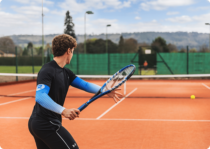 Man wearing black sportswear and blue compression sleeves, playing tennis on an outside court